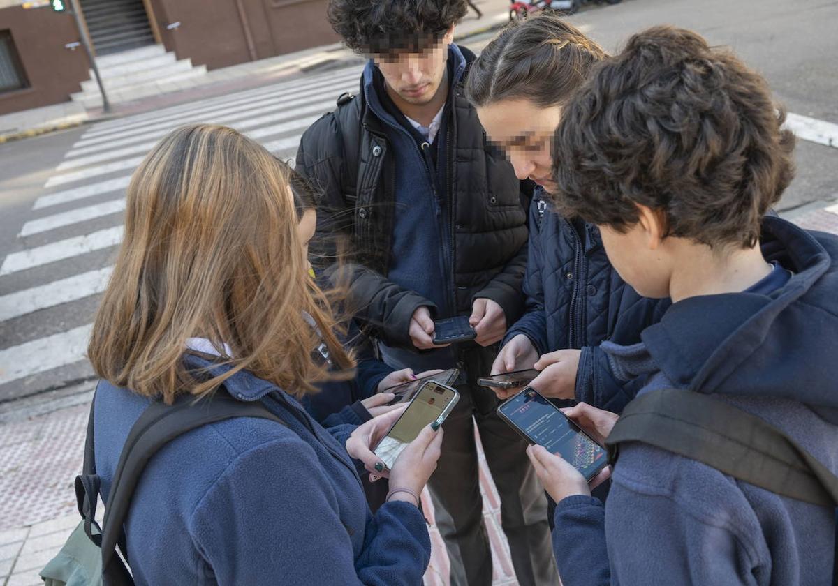 Adolescentes usando teléfonos móviles en la puerta de un centro educativo.