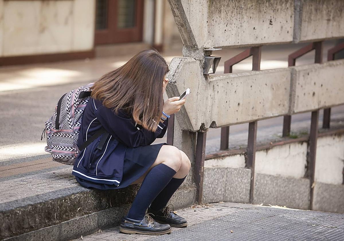 Una menor usa un móvil en la puerta de un centro educativo.