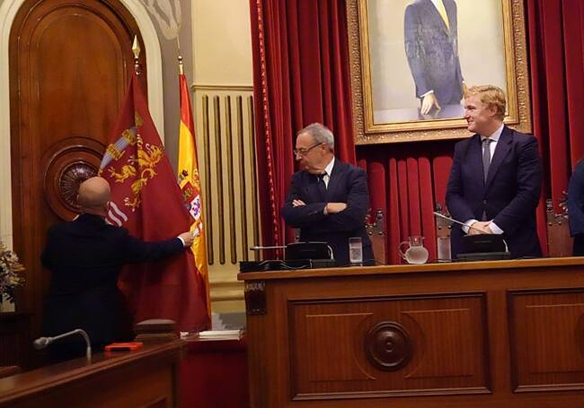 El alcalde, Ignacio Gragera, y el secretario del Ayuntamiento miran la colocación de la bandera en el salón de plenos el día de su aprobación en octubre de 2023.
