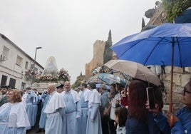 La procesión avanza hacia Fuente Concejo por San Roque, con los paraguas en primer plano y la imagen protegida de la lluvia.