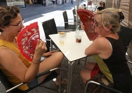 Dos mujeres abanicándose en una terraza.