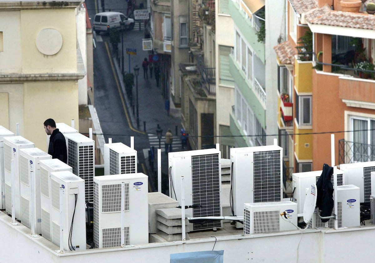 Un técnico revisa una instalación de aparatos de aire acondicionados en una azotea de pisos.