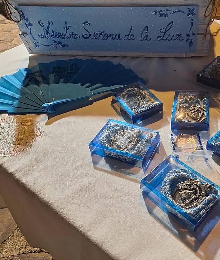Imagen secundaria 2 - Arriba, componentes del Coro de Nuestra Señora de los Santos de Táliga, que amenizarán con la misa extremeña la eucaristía de este 15 de agosto. Abajo, lona de las fiestas patronales y merchandising que pone en venta la Hermandad de la Virgen de la Luz.