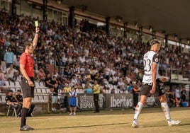 El colegiado Manuel Camacho Garrote mostrando la tarjeta amarilla al jugador del Mérida Busi.