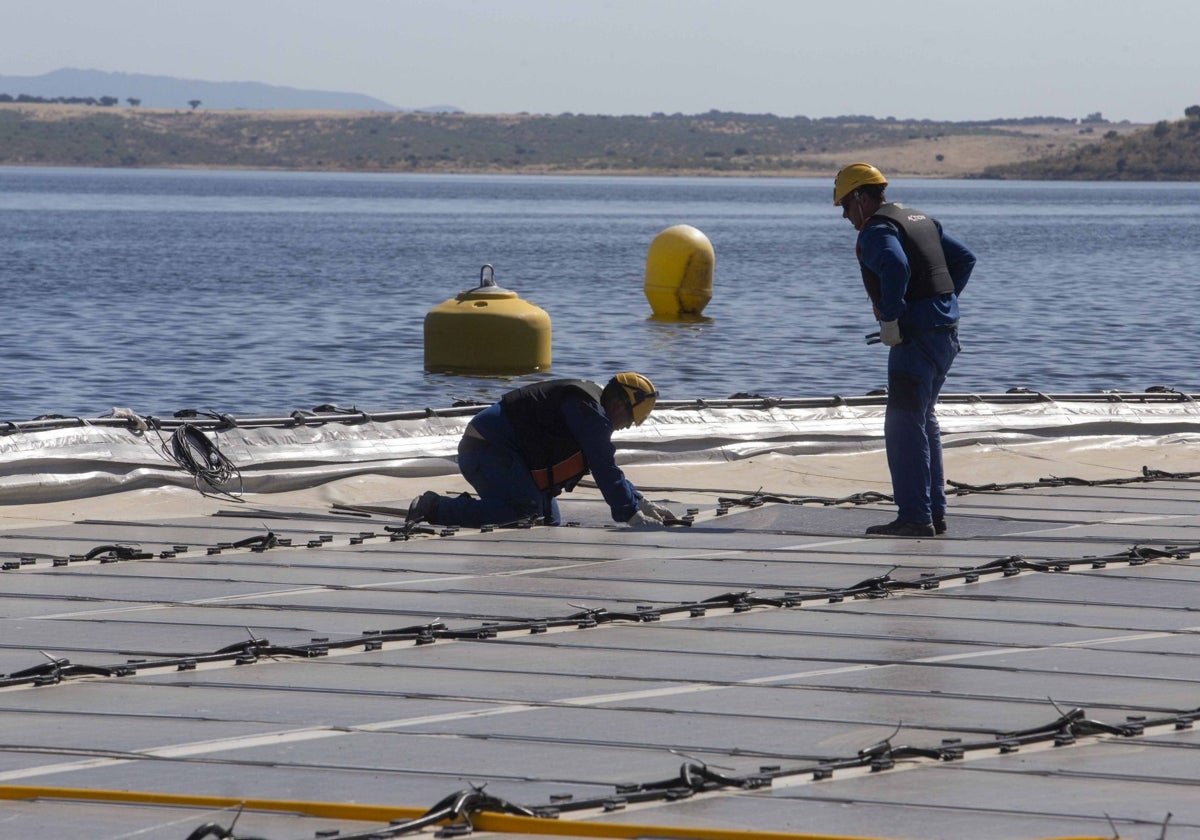 Dos operarios colocan un panel solar en la planta fotovoltaica flotante de Sierra Brava, en Zorita.