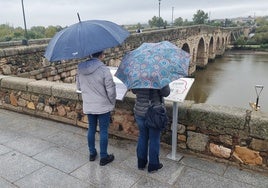 Dos turistas, la pasada semana, junto al Puente Romano de Mérida en una jornada lluviosa.