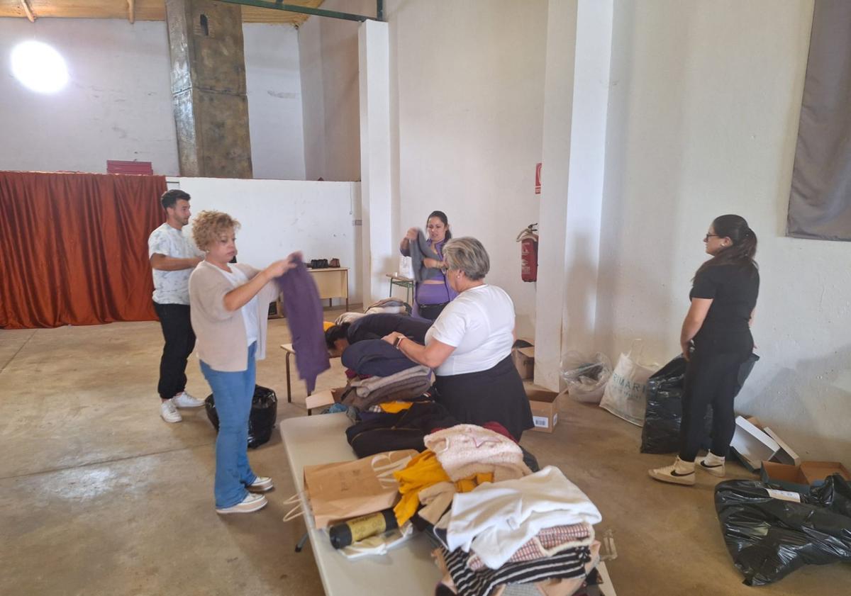 Imagen principal - Arriba, grupo de voluntarias, este lunes, clasificando y emaquetando ropa. Abajo, a la izquierda, primeros palés y cajas de productos. A la derecha, taza solidaria que se pondrá en venta.