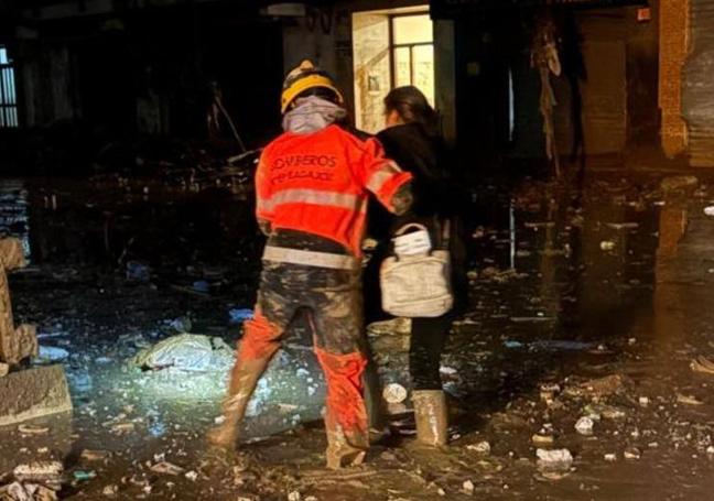 Un bombero de la Diputación de Badajoz ayuda a una mujer a caminar entre el lodo.