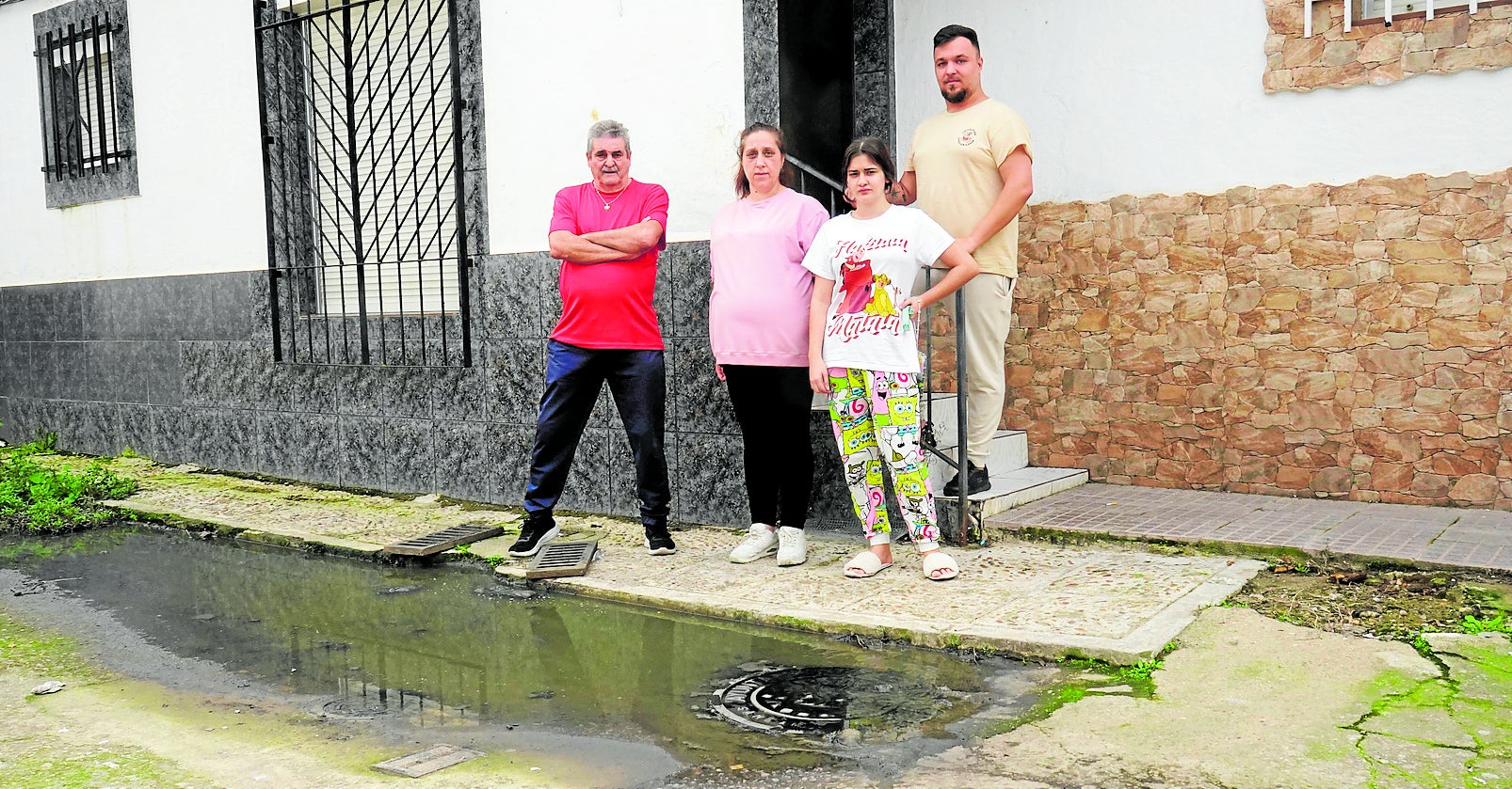 Soledad Jiménez junto a sus vecinos en la puerta de su casa, donde no deja de salir agua sucia del colector.