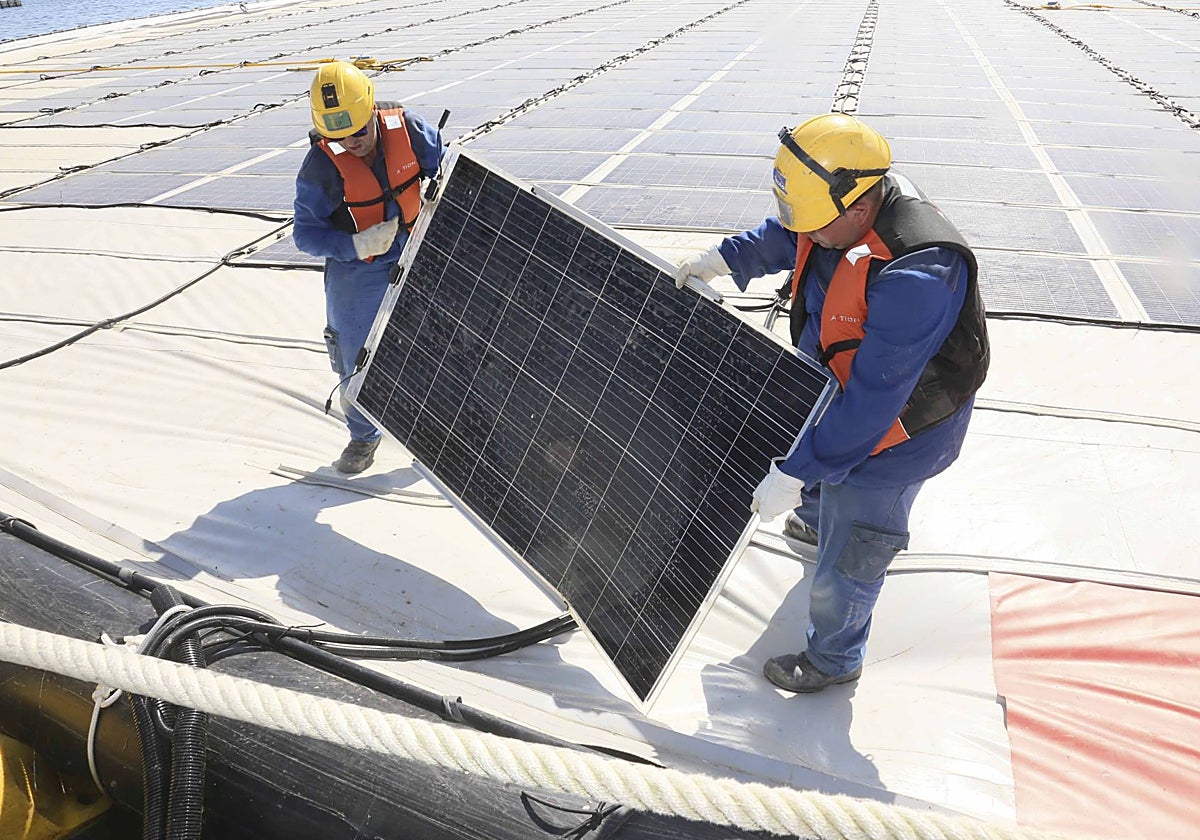 Dos operarios colocan paneles solares para autoconsumo en la fotovoltaica flotante de Sierra Brava.