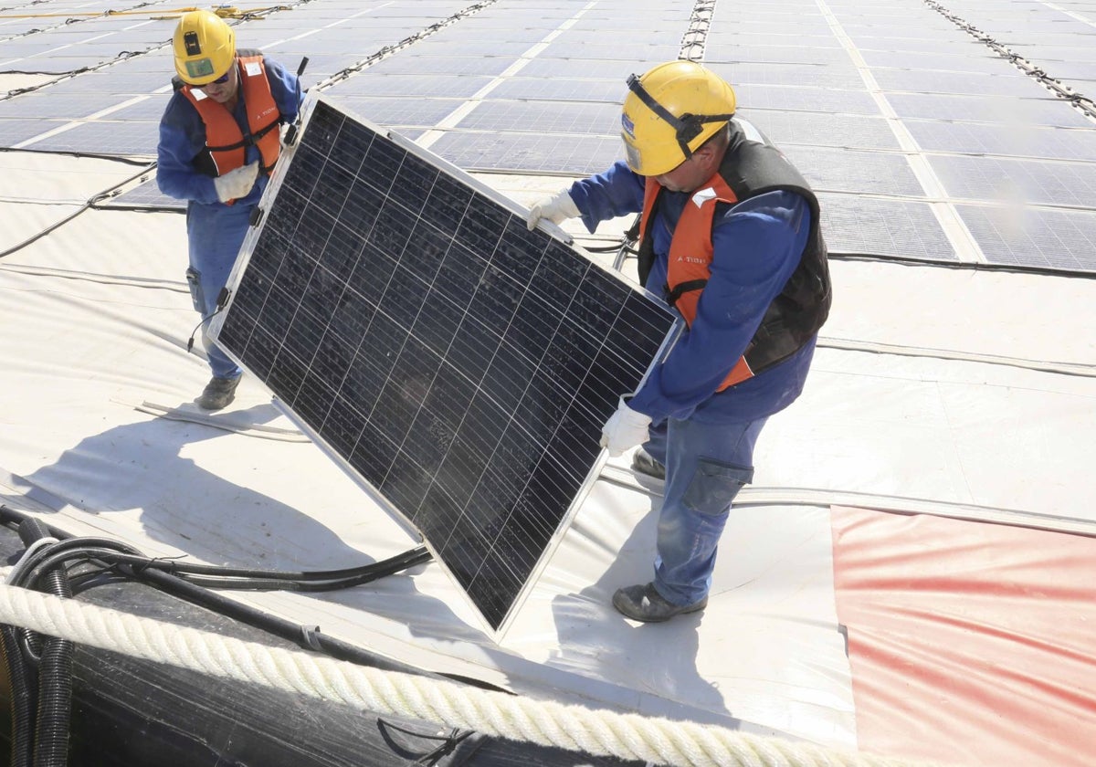 Dos operarios instalan un panel solar en una fotovotaica para autoconsumo sobre el embalse de Sierra Brava, en la localidad cacereña de Zorita.