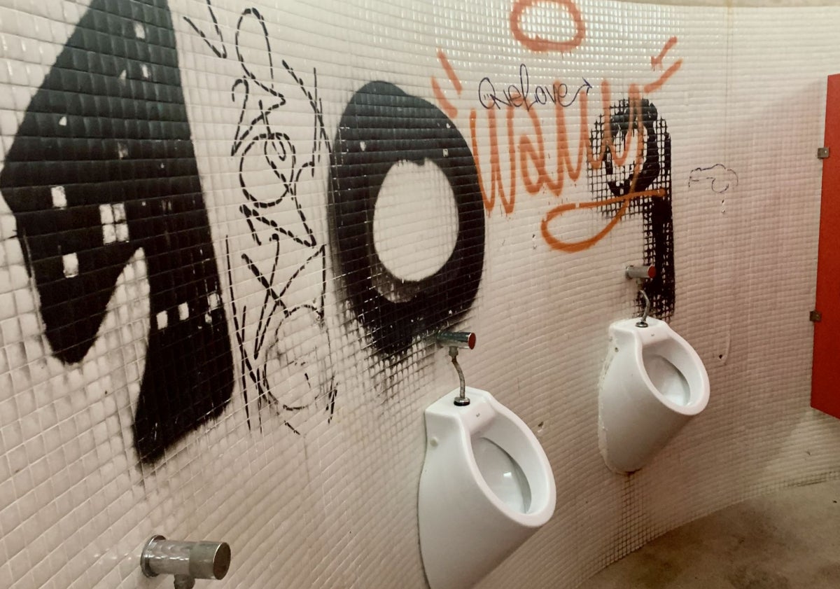 Imagen principal - La zona de los urinarios, afectada. La de los lavabos sin espejo, por haber desaparecido, una parte del mobiliario deteriorada y el servicio sin tapadera.