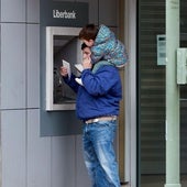 Un padre con su hijo saca dinero de un cajero.