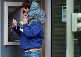 Un padre con su hijo saca dinero de un cajero.