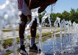 Una persona se refresca en una fuente pública.
