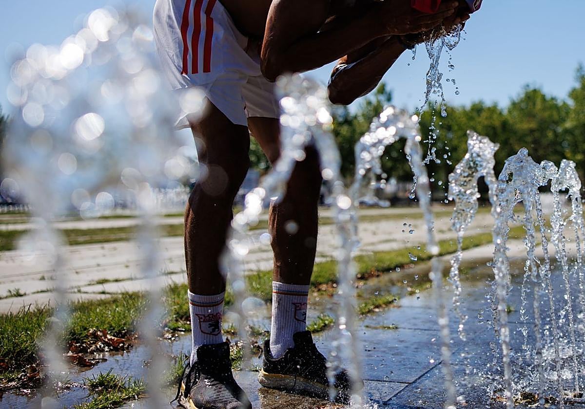 Una persona se refresca en una fuente pública.