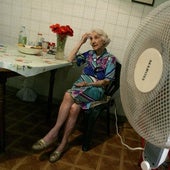 Una mujer mayor climatiza su casa con un ventilador.
