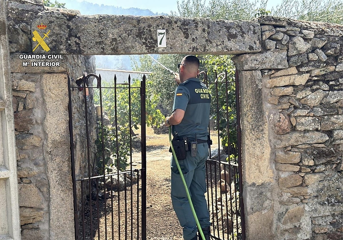 Un guardia civil refresca un huerto para intentar minimizar daños si llega el fuego.