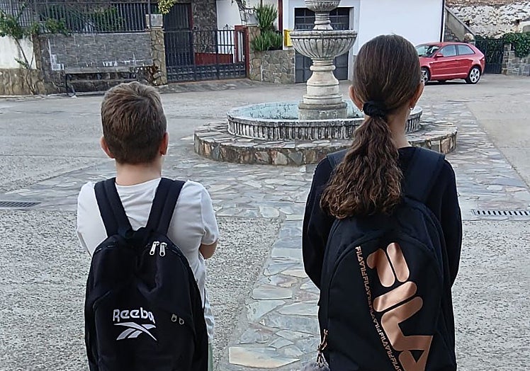 Dos niños de Cambroncino esperando sin éxito en la parada del autobús que le debería llevar al colegio de Caminomorisco.