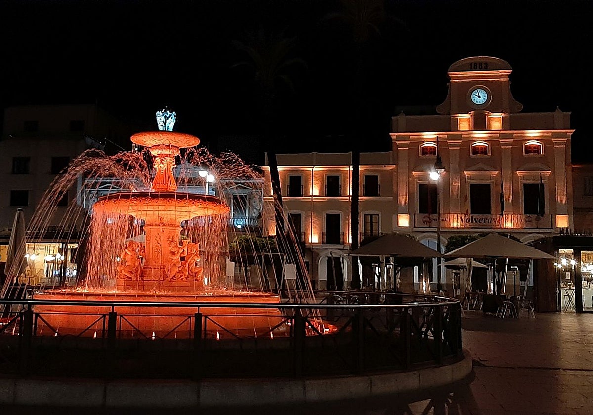 Fuente de la plaza de España y fachada del Ayuntamiento, iluminadas con color naranja.