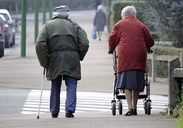 Una pareja de ancianos con problemas de movilidad caminan por la calle.