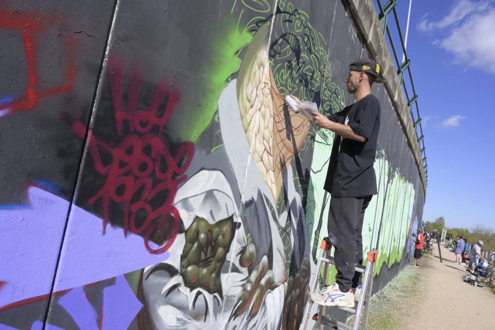 El artista pacense Alejandro Pajuelo, alias Chino, crea un cocodrilo-humano junto al Guadiana tras escribir, en rojo, 'HOY Desde 1933', en alusión a este diario.