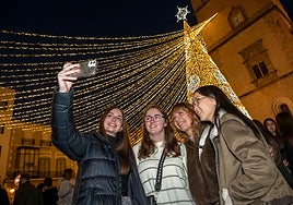Unas jóvenes se hacen fotos con la guirnalda de luces de fondo, sujetas a la torre de la Catedral.