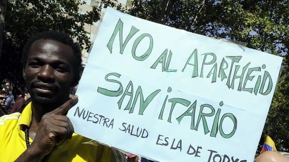 Un hombre sostiene un cartel contra los recortes en sanidad que afectan a la atención de los extranjeros irregulares.