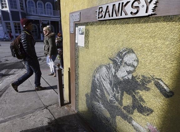 Transeúntes pasan junto al muro de un edificio, en Park City (Utah), adornado con una obra de Banksy.
