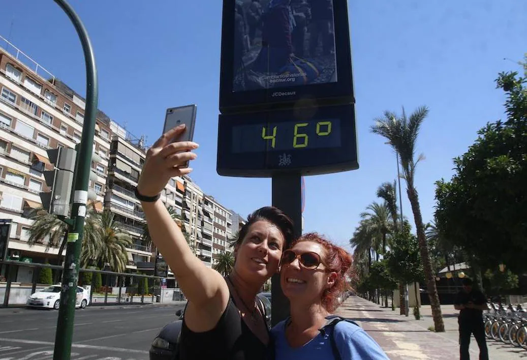 Dos jóvenes se hacen una foto con el panel del termómetro de una calle de Córdoba. 