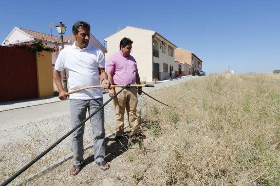 Dos de los afectados sujetan con un palo el cable por el que llega la electricidad a sus casas. :: andy solé