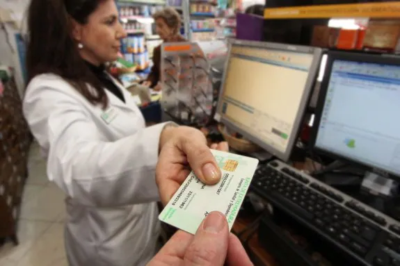Un usuario entrega su tarjeta para que la farmacéutica acceda a su receta electrónica. :: andy solé