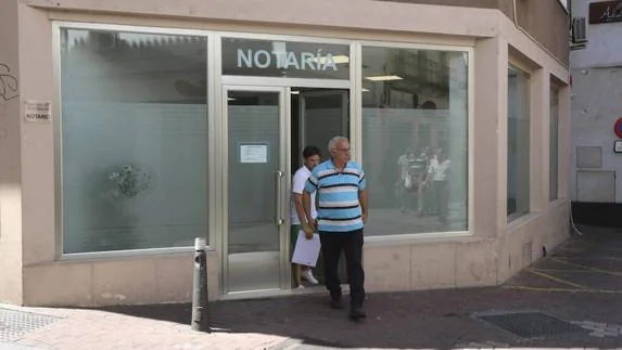 Dos personas salen de la notaría situada en la calle Los Maestros de Mérida.