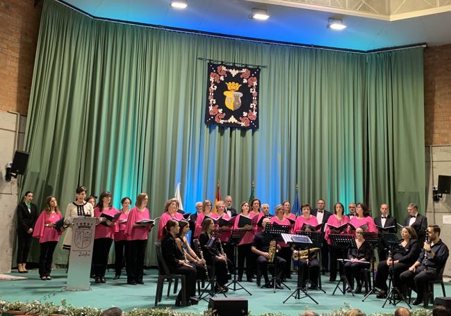 La presentadora del acto junto a la coral y el gruo de Cámara de la Bande de Música