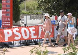 Unas personas caminan junto a una pancarta del PSOE de Mojácar.