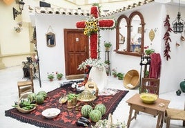 Imagen de una cruz de mayo con sandías y flores alrededor.