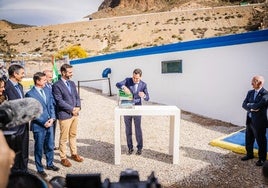 El presidente de la Junta sostiene una bandera de Andalucía ante la atenta mirada de varias autoridades.