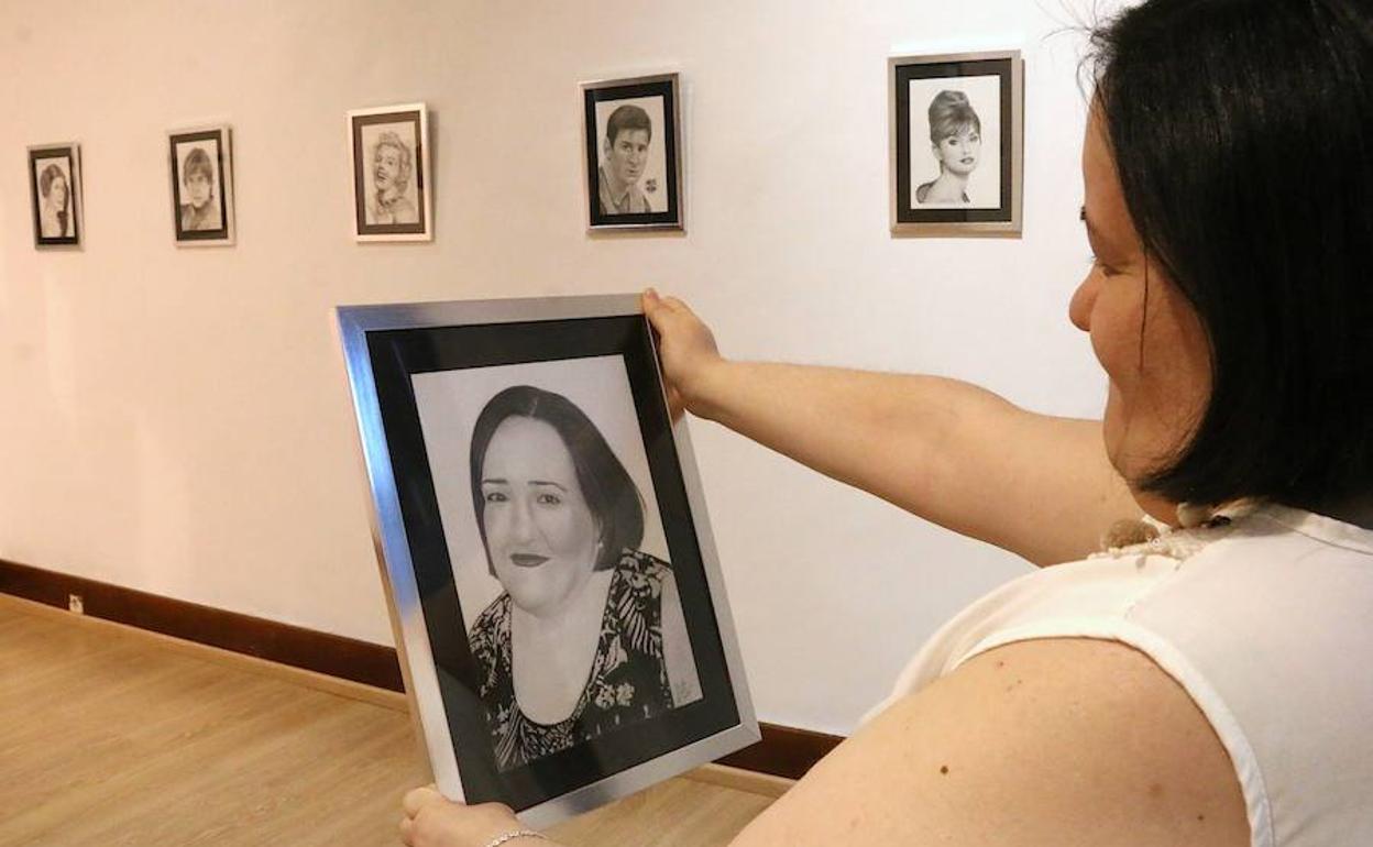Paula López frente a su autorretrato y ante algunas de sus obras.