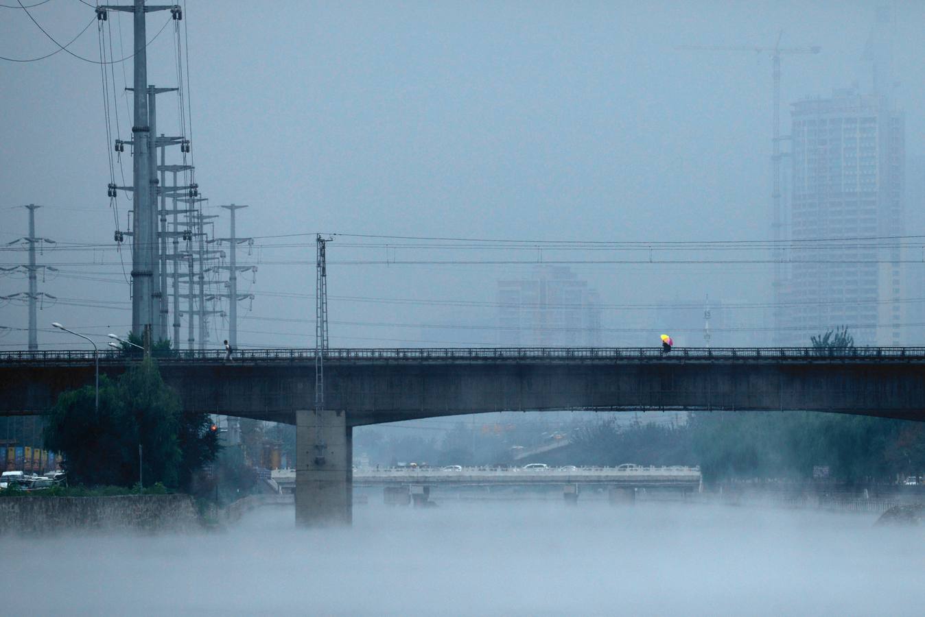 Un hombre sostiene un paraguas mientras camina sobre un puente en Beijing.