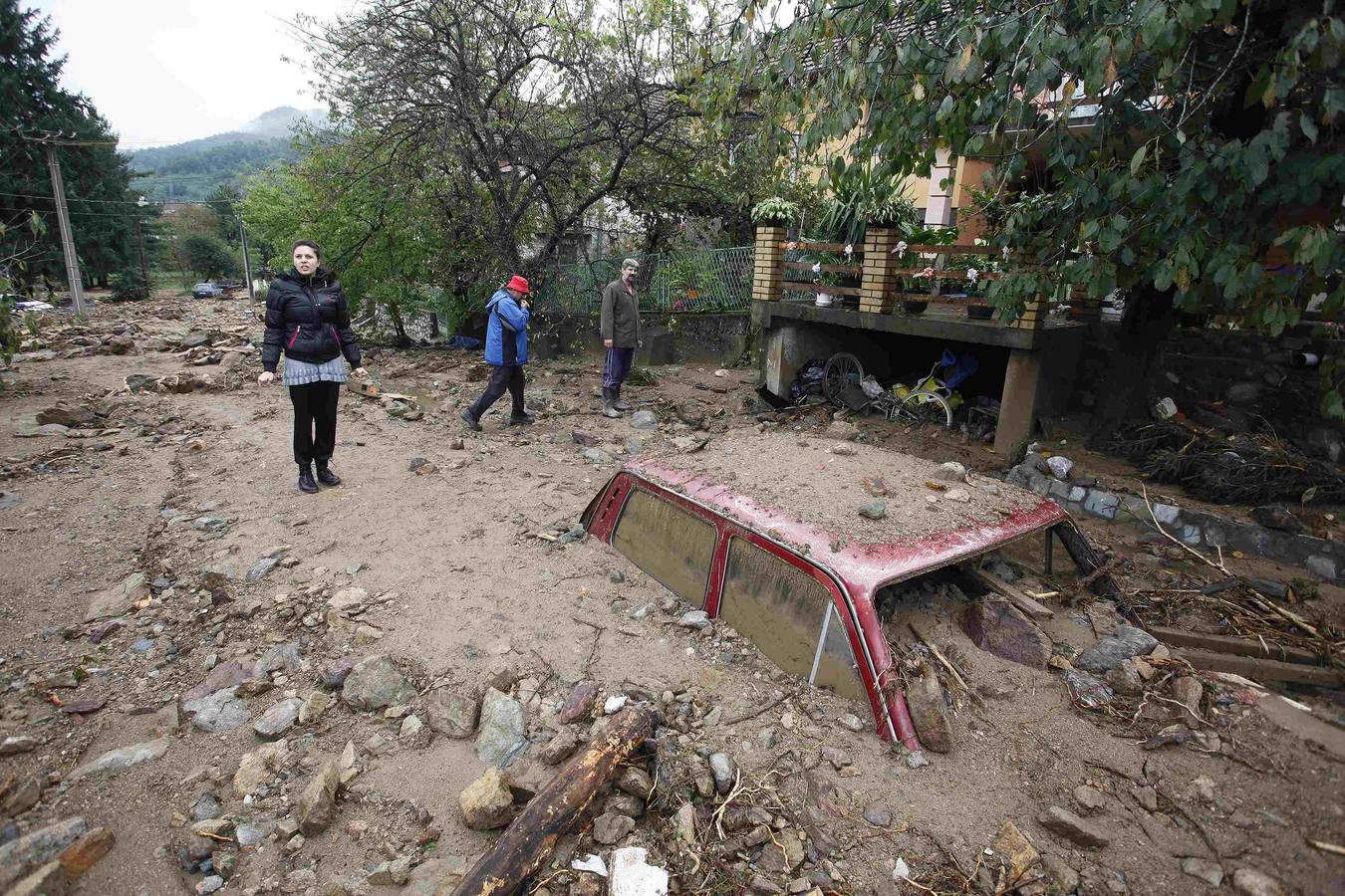 La gente pasa por un vehículo casi completamente sumergida en una calle cubierta de barro debido a las fuertes inundaciones en la aldea Tekija.