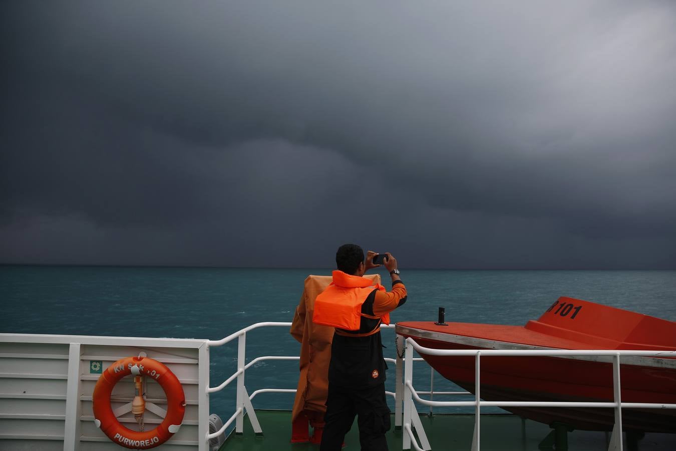 Un miembro del equipo de rescate toma una imagen de mal tiempo en la cubierta de la Búsqueda y Salvamento, en una operación de búsqueda de los pasajeros a bordo del vuelo de AirAsia.