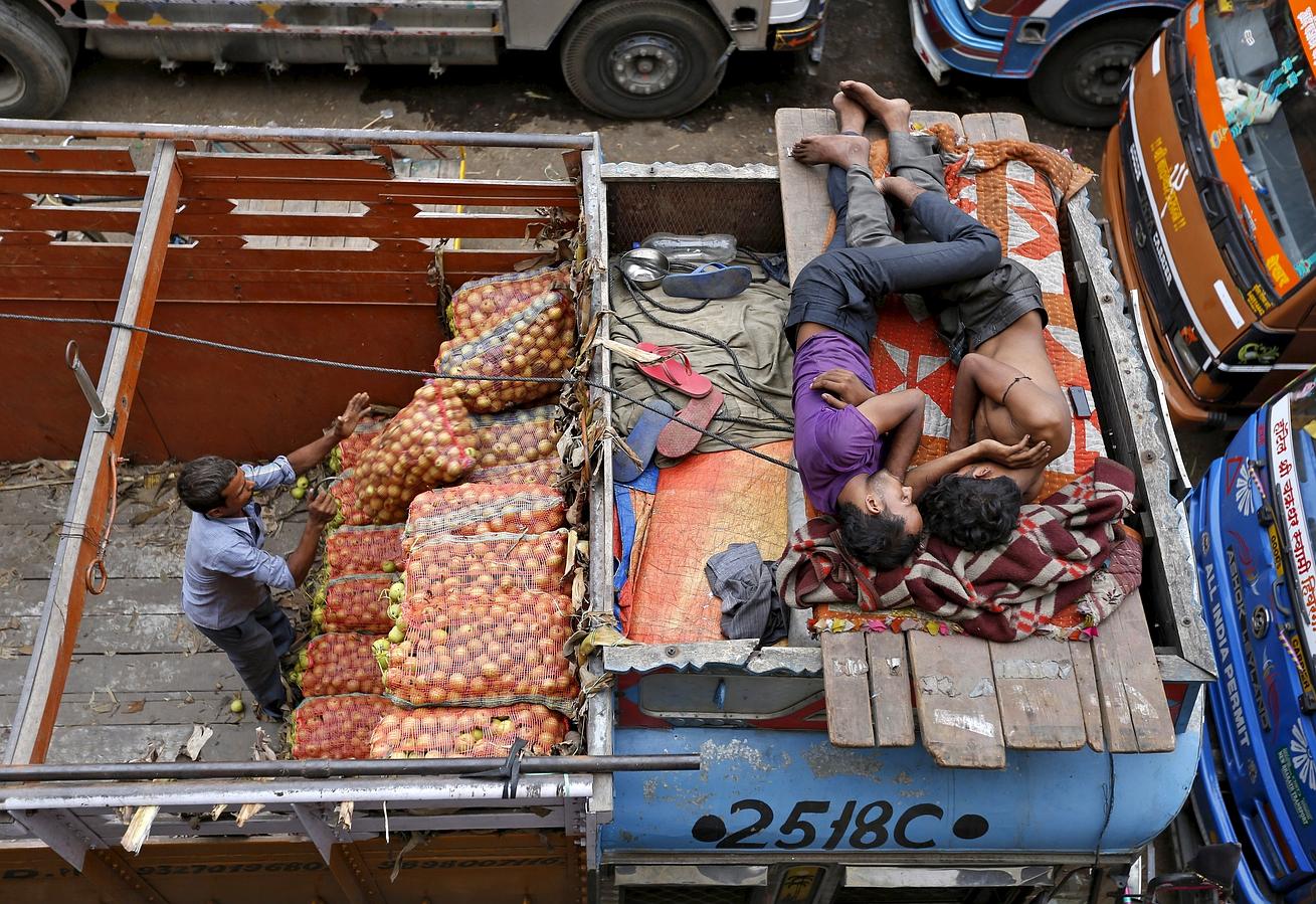 Un trabajador descarga sacos de verduras mientras dos hombres duermen en la parte superior de un camión.
