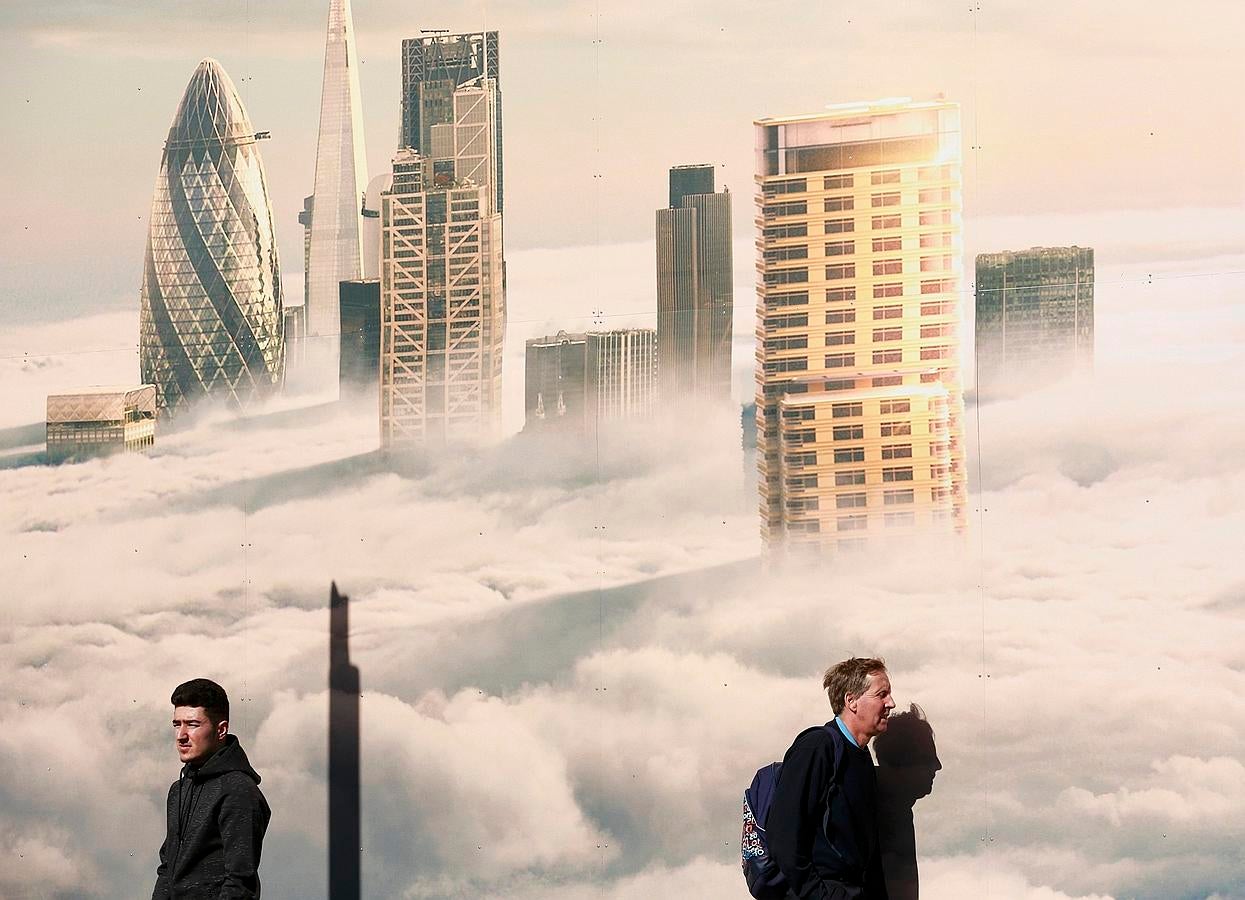 Los hombres pasan junto a una imagen de la ciudad envuelta en niebla, en un día soleado de primavera en Londres.