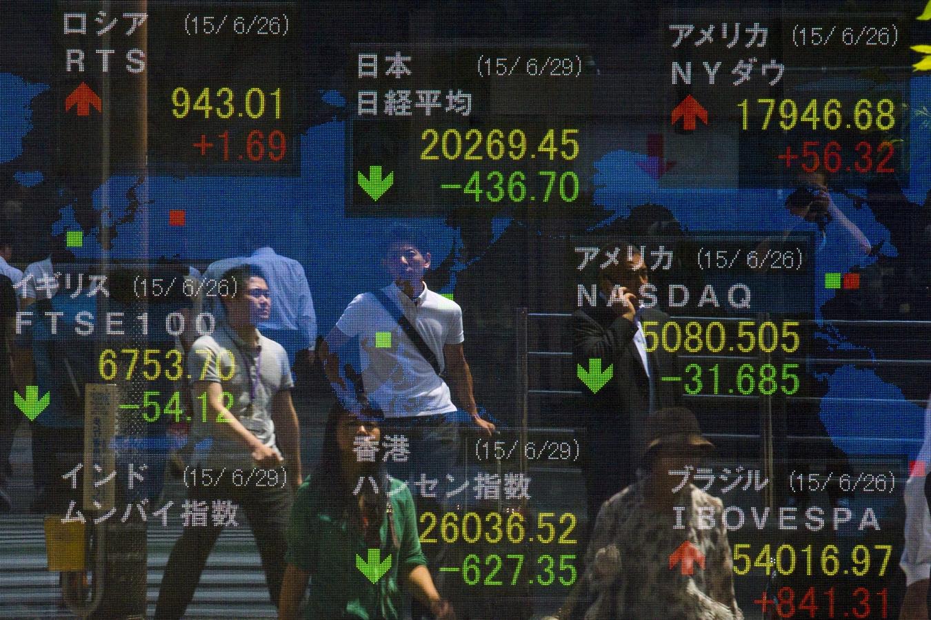 La gente se para delante de una pantalla que muestra el promedio Nikkei y otros índices del mercado en Tokio 29 de junio de 2015.