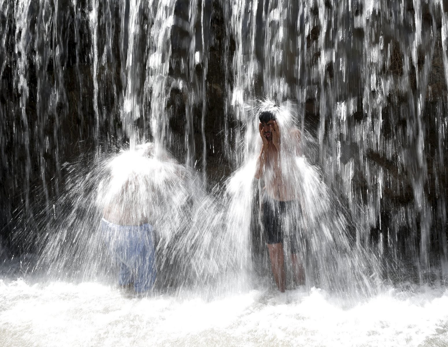 Hombres afganos se lavan bajo una cascada para refrescarse en la provincia de Parwan, Afganistán.