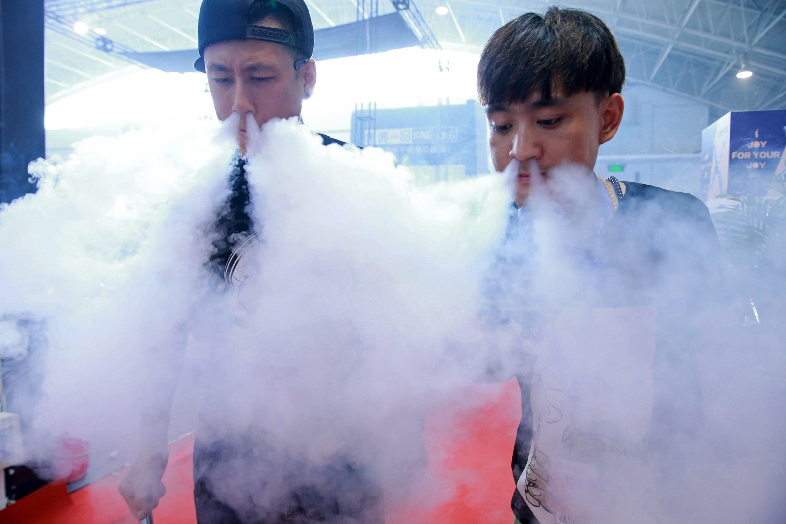 Esta imagen muestra personal de ventas exhalando vapores de cigarrillos electrónicos al tiempo que muestran sus productos en el Beijing International Vapor Distribution Alliance Expo, o el Vape de China Expo, en el China International Exhibition Center en Beijing.