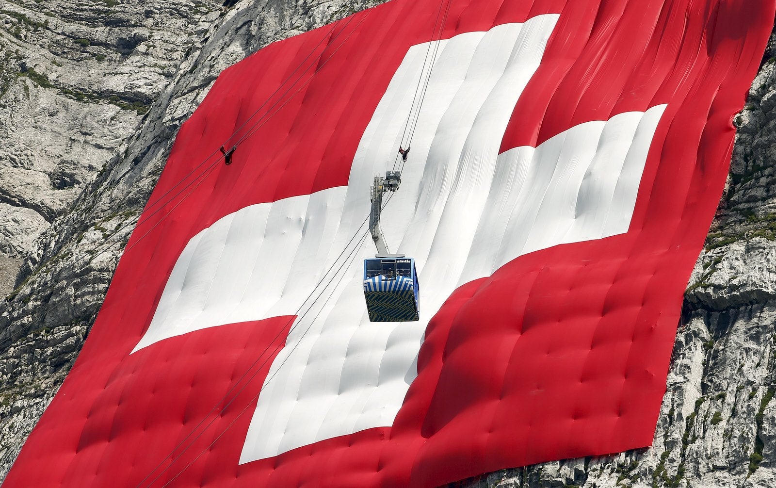 Descenso de un Teleférico en frente de un enorme bandera nacional de Suiza.