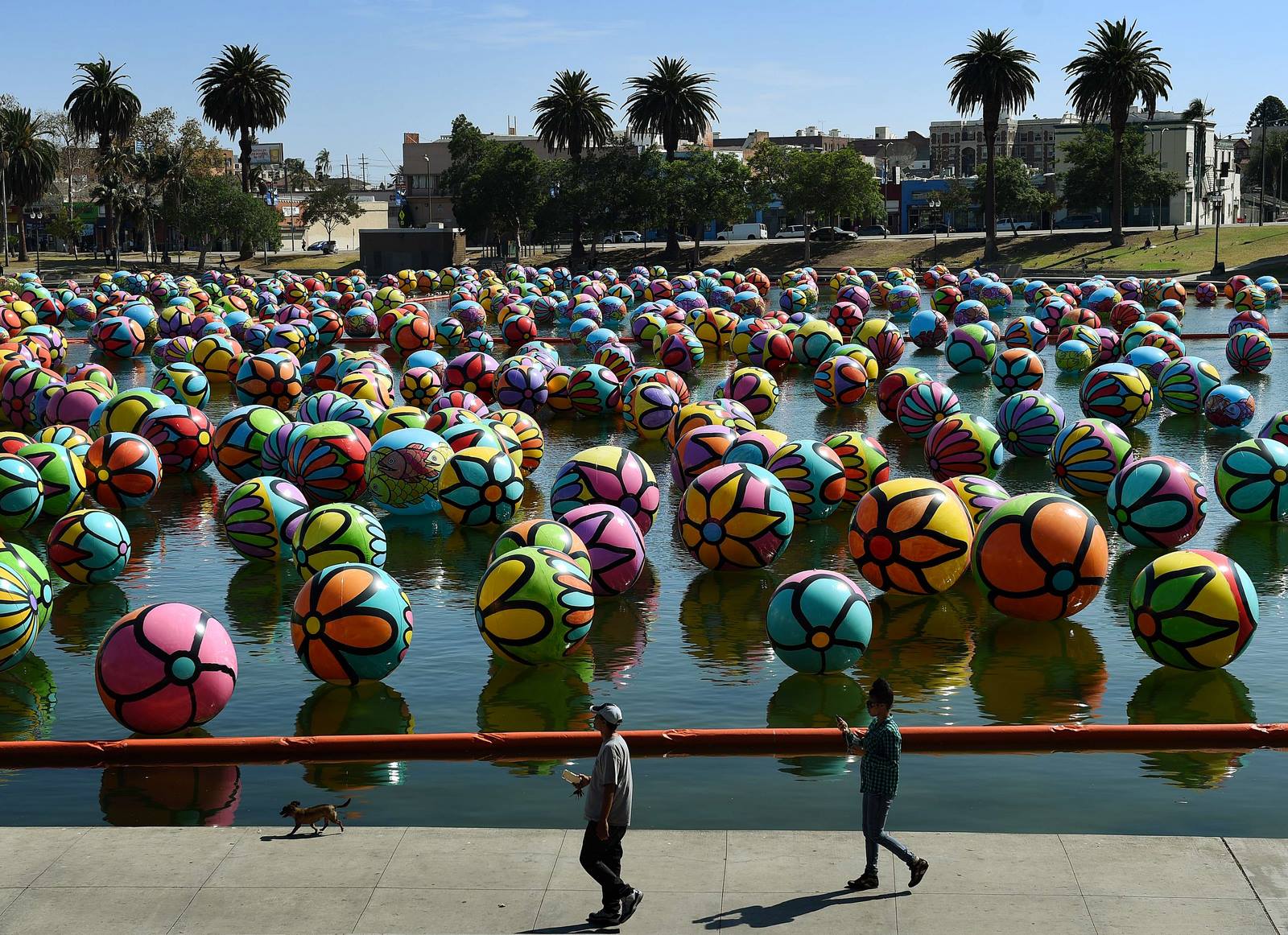 Gente camina entre bolas de vinilo pintados a mano que flotan en el lago del Parque MacArthur.