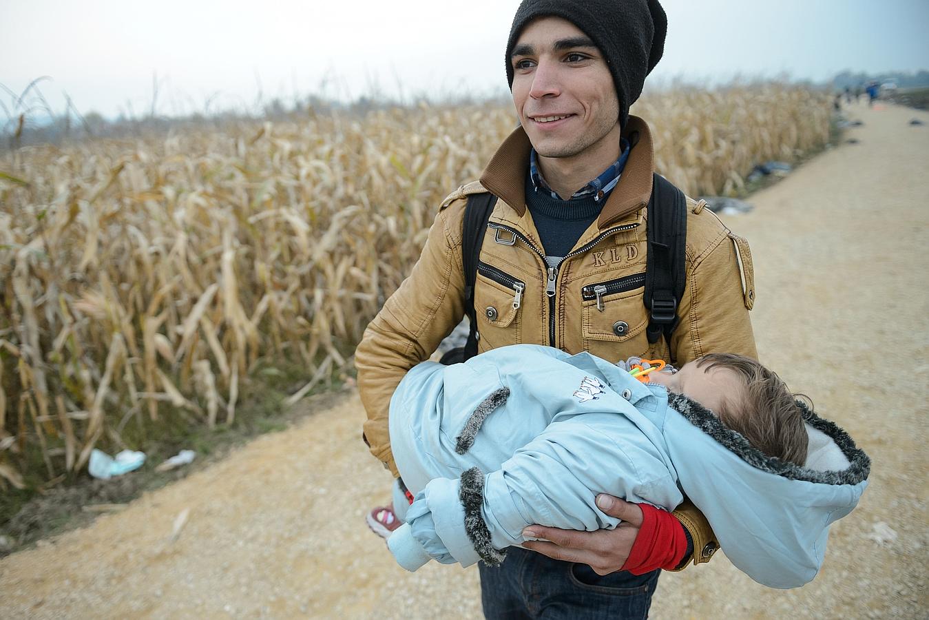 Un inmigrante lleva un niño hacia los autobuses que deben tomar para llegar a uno de los centros de refugiados después de cruzar la frontera croata-esloveno en Rigonce.