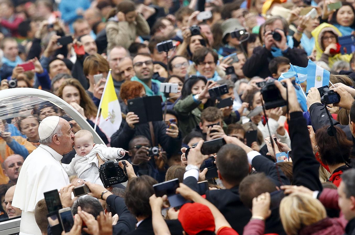 El papa Francisco besa a un bebé a medida que llega a la audiencia semanal en la Plaza de San Pedro en el Vaticano.